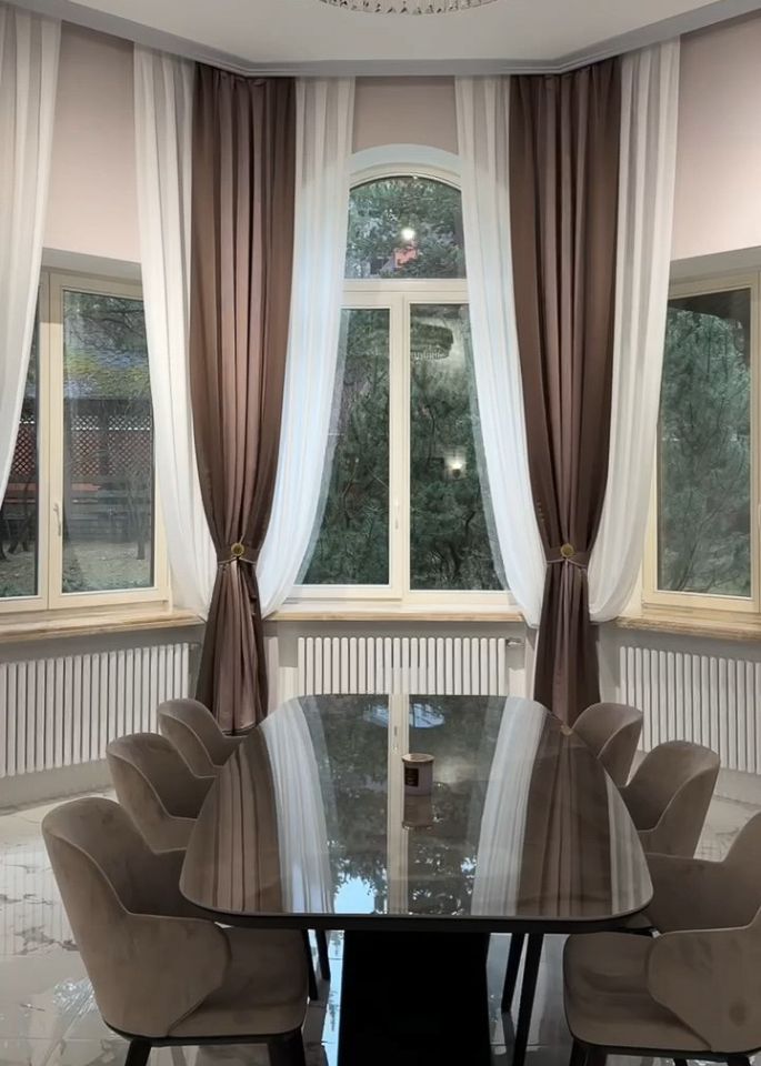 Обеденная зона в классическом стиле, арочное окно со шторами двух цветов: белыми полупрозрачными и плотными коричневыми.